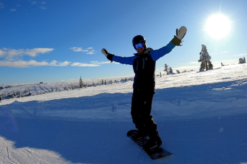 Me at the top of a slope on a snowboard in sunny weather.